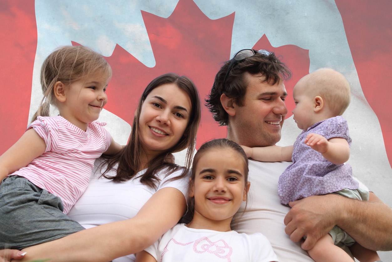 Young family of Mother, Father holding their three children in front of the Canadian Flag