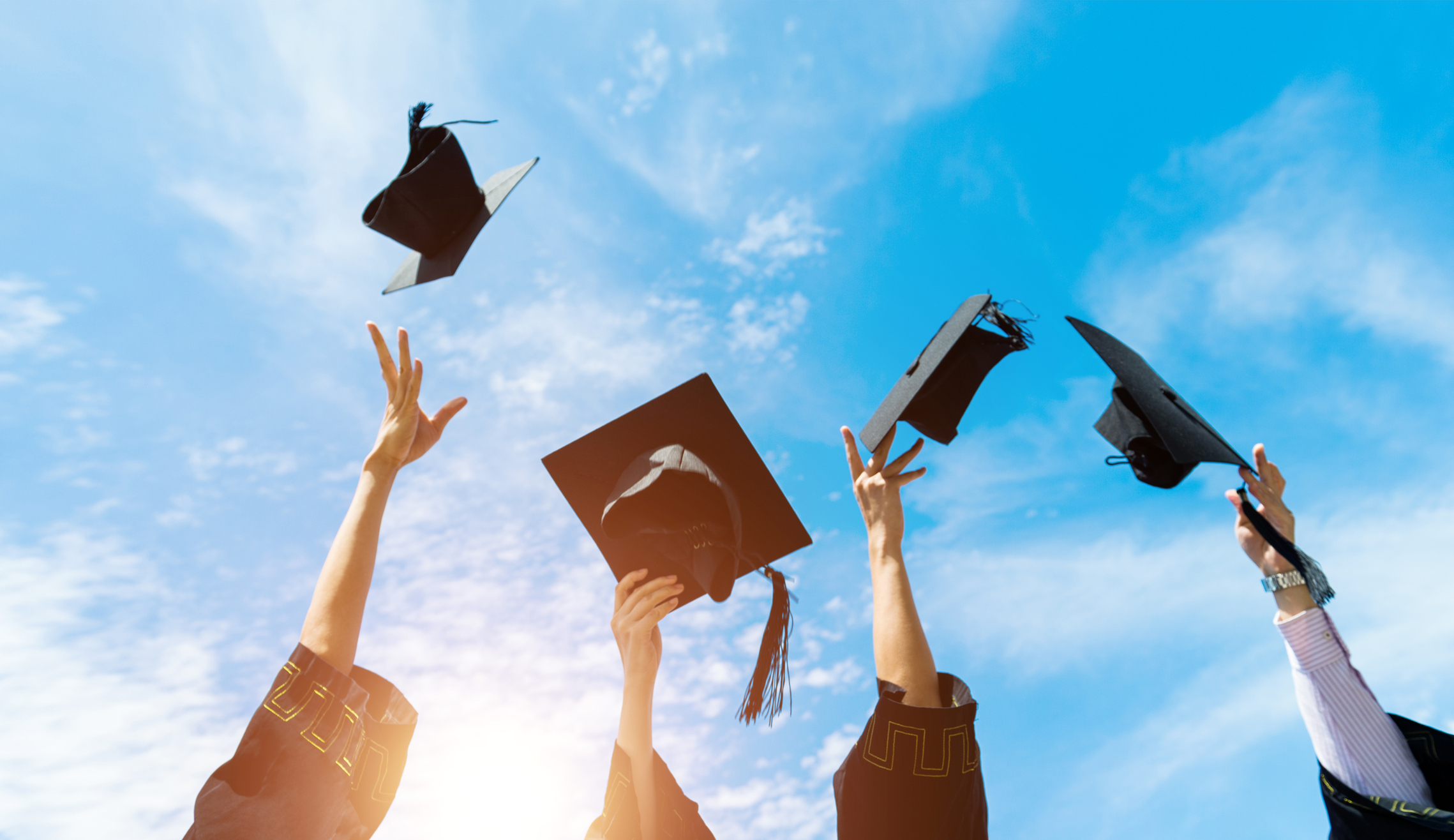 Four graduates throwing graduation hats in the air