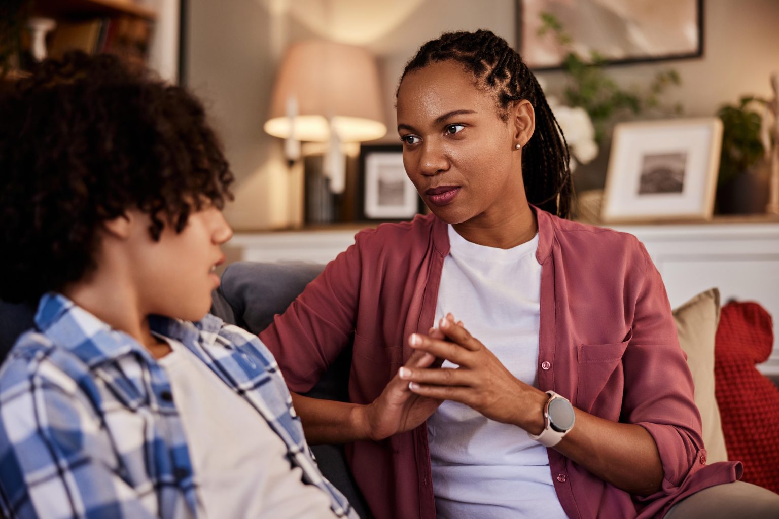 A pretty African-American mother and her teenage son talking while sitting on a couch at home.