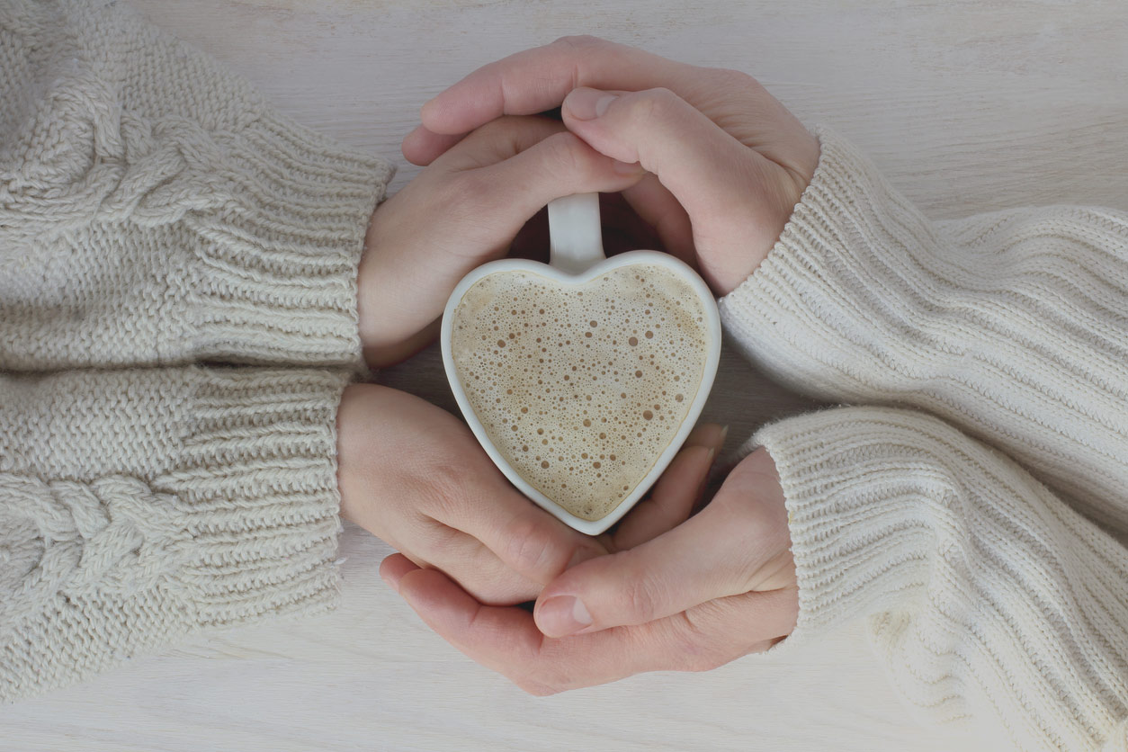 Symbolic photo of two pairs of hands wrapped around a heart shaped mug of hot coffee symbolizing blessing of forgiveness.