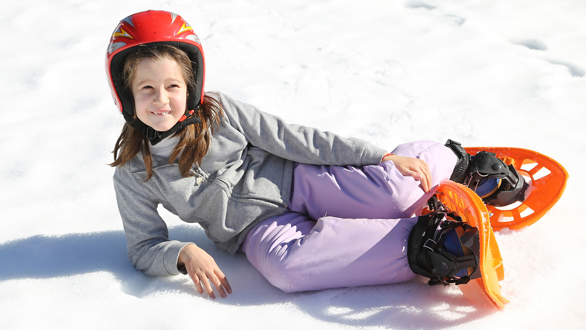 pretty girl with orange snowshoes on snow in winter