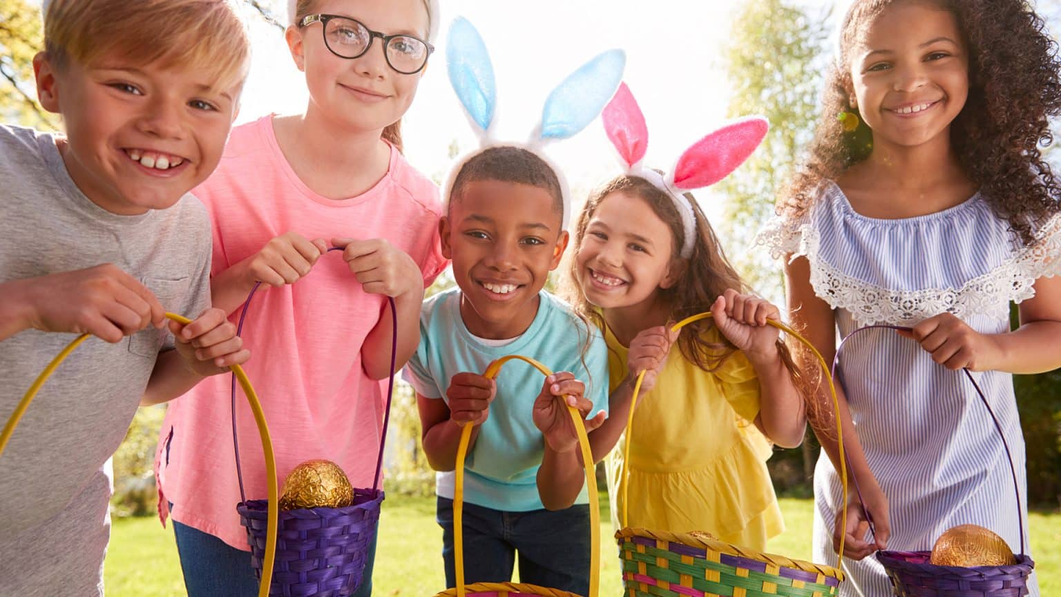 Portrait Of Five Children Wearing Bunny Ears On Easter Egg Hunt In Garden making Easter fun for Kids.