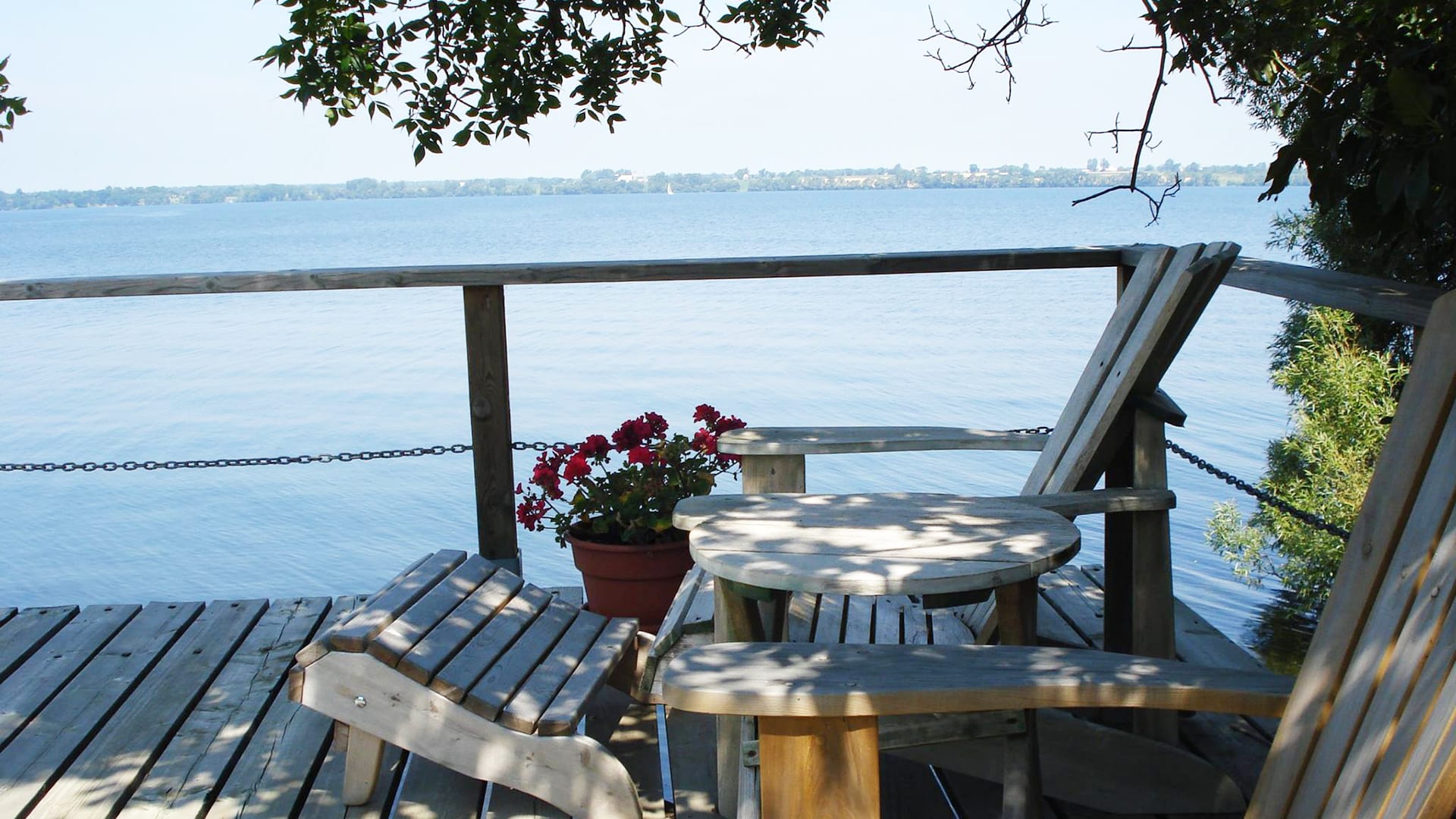 A photo of an Adirondak chair on a deck down by the water overlooking sailboats in the Bay of Quinte.