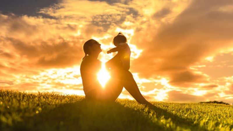 An image of a mother and her young child set against a backdrop of sunrise in early morning.
