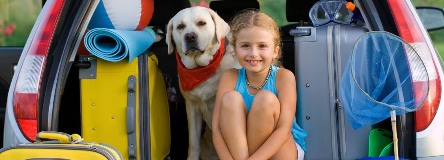 Young girl and her dog ready for the long weekend packing up the car for a camping trip on the Victoria Day Long Weekend.