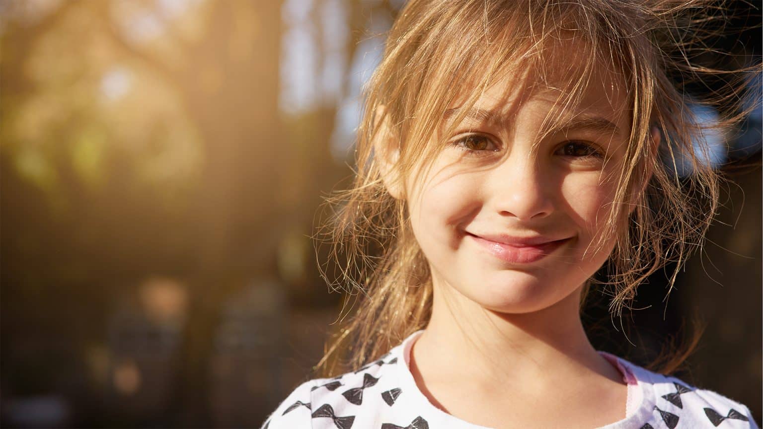 Photo of a shy young girl looking directly at the camera smiling.
