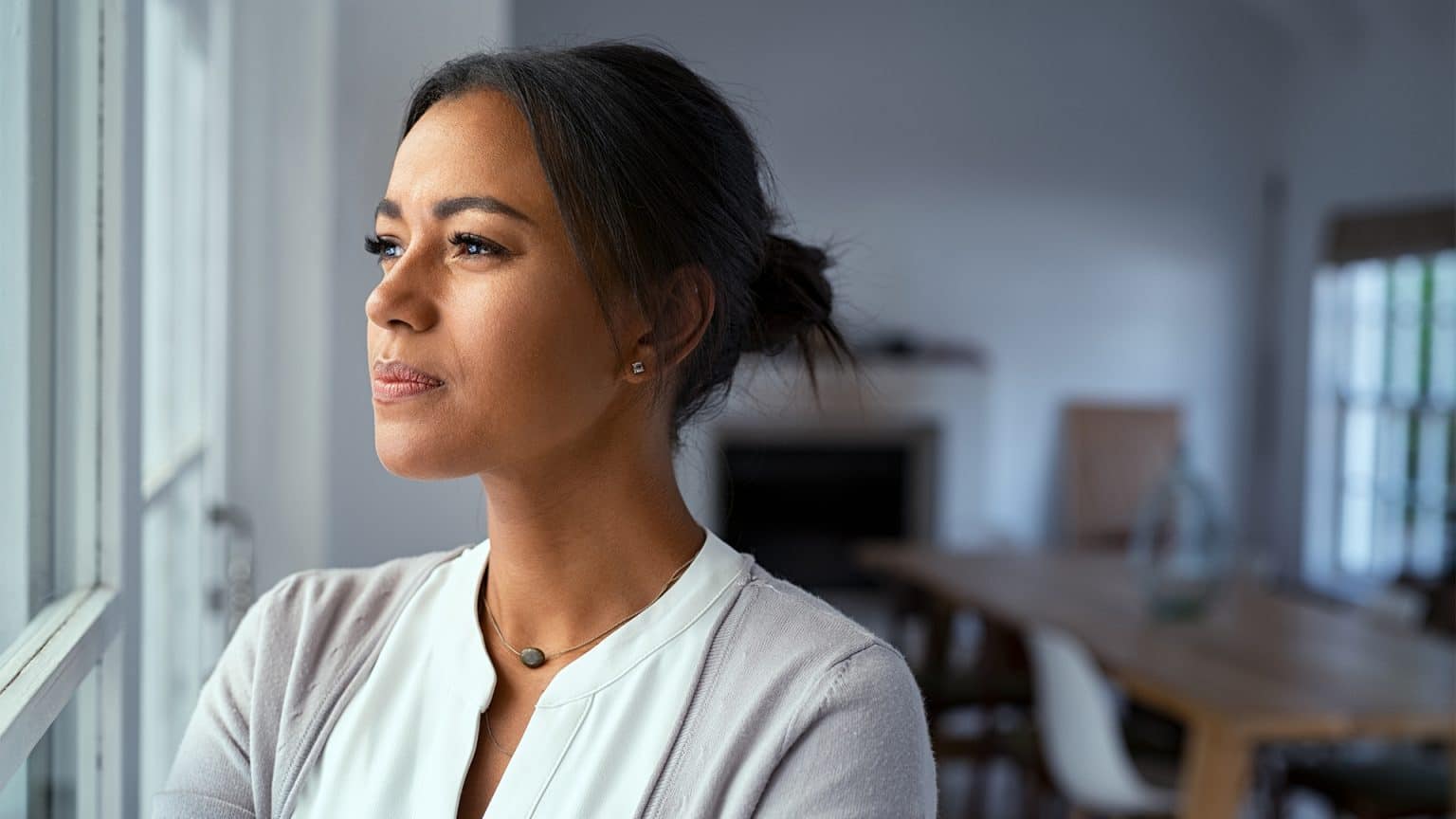 A pensive woman at home worried about change in her life looking out a window.