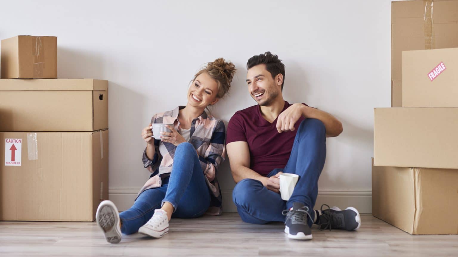 Happy couple with coffee cups relaxing in their new home after moving.