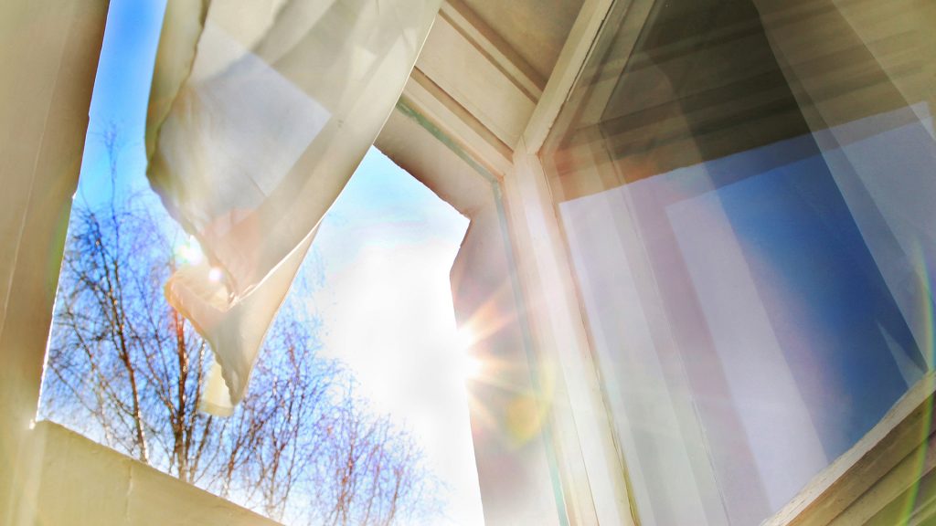 Open window letting in the light. this is a positive and hopeful feeling image. Light wind blows to open window and sways thin curtain against sunshine at summer or spring day