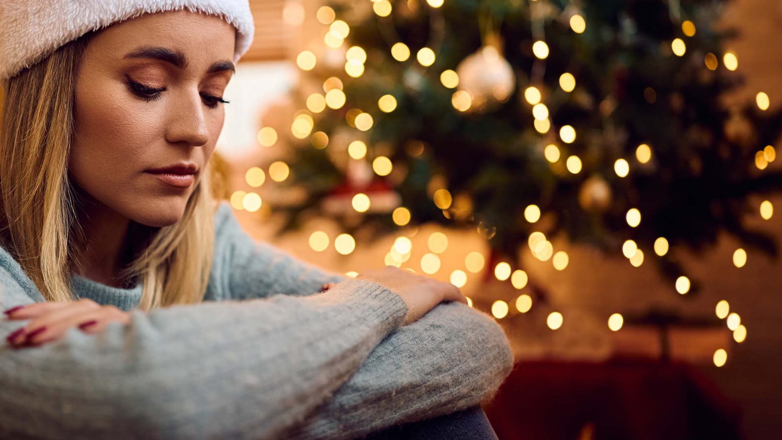 Woman looking and feeling sad and lonely sitting beside the Christmas Tree.